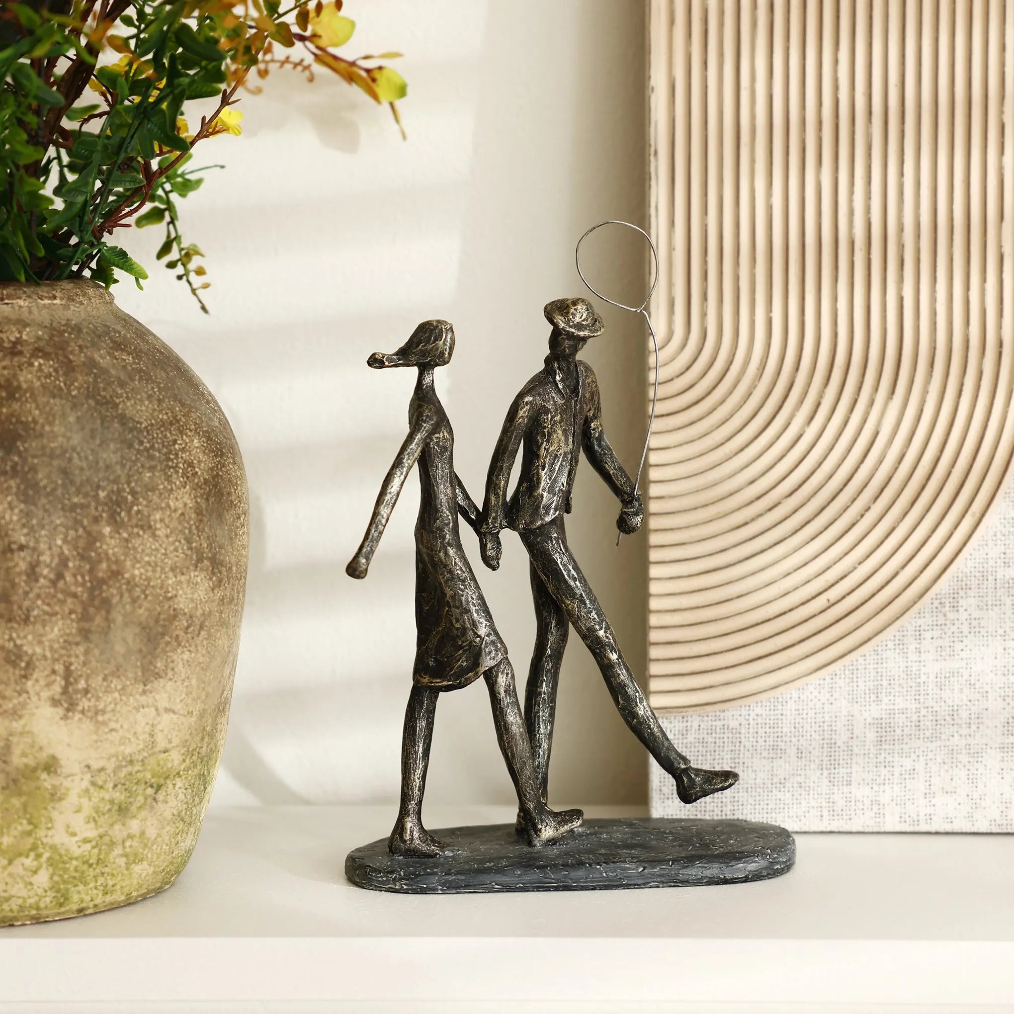 A metal sculpture of a couple walking hand in hand is displayed on a shelf, complemented by a large, textured vase and decorative artwork, creating a stylish modern resin home decoration ensemble.