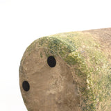 Close-up of the end of a rustic, moss-covered object with two black circular spots on its surface, set against a white background.