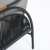 Close-up of a modern chair featuring a metal frame with a woven backrest and wooden armrest accents, designed as part of an elegant outdoor seating set. Enhance comfort with its removable waterproof cushions, perfect for enjoying the open air in style.