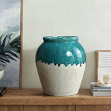A large ceramic vase with a glossy turquoise upper section and a textured white lower section sits on a wooden table next to books and a candle, echoing the charm of rustic design.