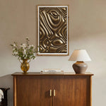 A wooden cabinet hosts a vase of flowers, a stack of books, and a lamp, while gold metal abstract wall decor adds flair above on the beige wall.