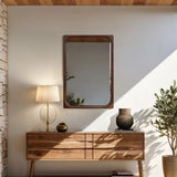 Modern interior with a sleek wooden sideboard and a round table lamp. A striking wall mirror with a rubberwood frame hangs prominently above. A potted plant basks in sunlights glow, embodying refined home decor.