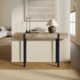 A modern farmhouse console table made of high-quality manufactured wood with black metal legs stands against a beige wall, topped with a lamp, two candleholders, and a book in a minimalist living space.