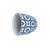 A blue and white ceramic cup, reminiscent of a modern planter, lies on its side, showcasing circular floral patterns.