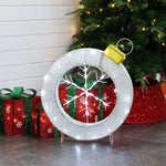 A large, illuminated snowflake wreath serves as a stunning holiday decoration in front of a Christmas tree. Two glittery gift boxes are positioned nearby, completing the enchanting Christmas decor.