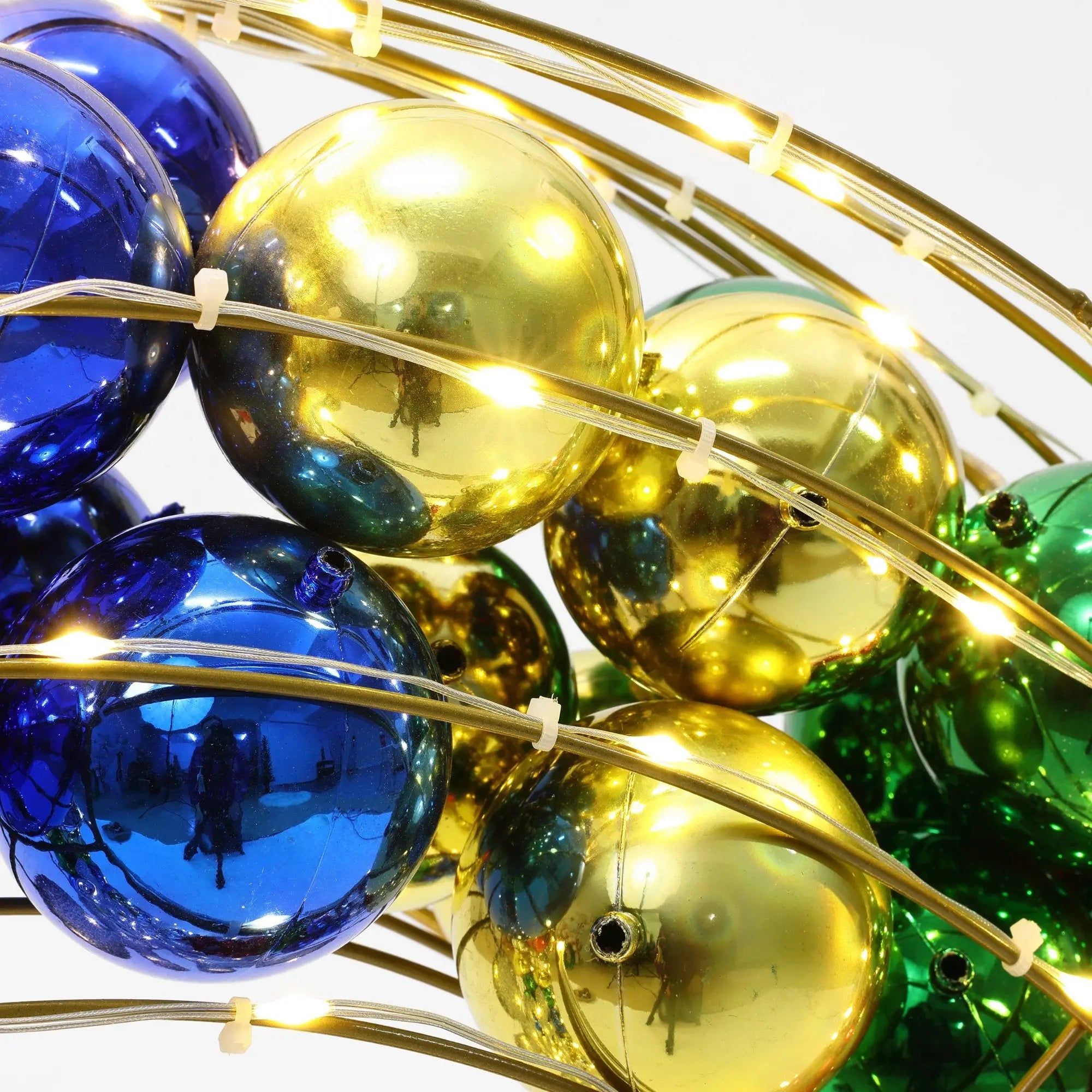 Close-up of shiny blue, gold, and green spheres interwoven with string lights on metal arches creating a festive holiday decoration.