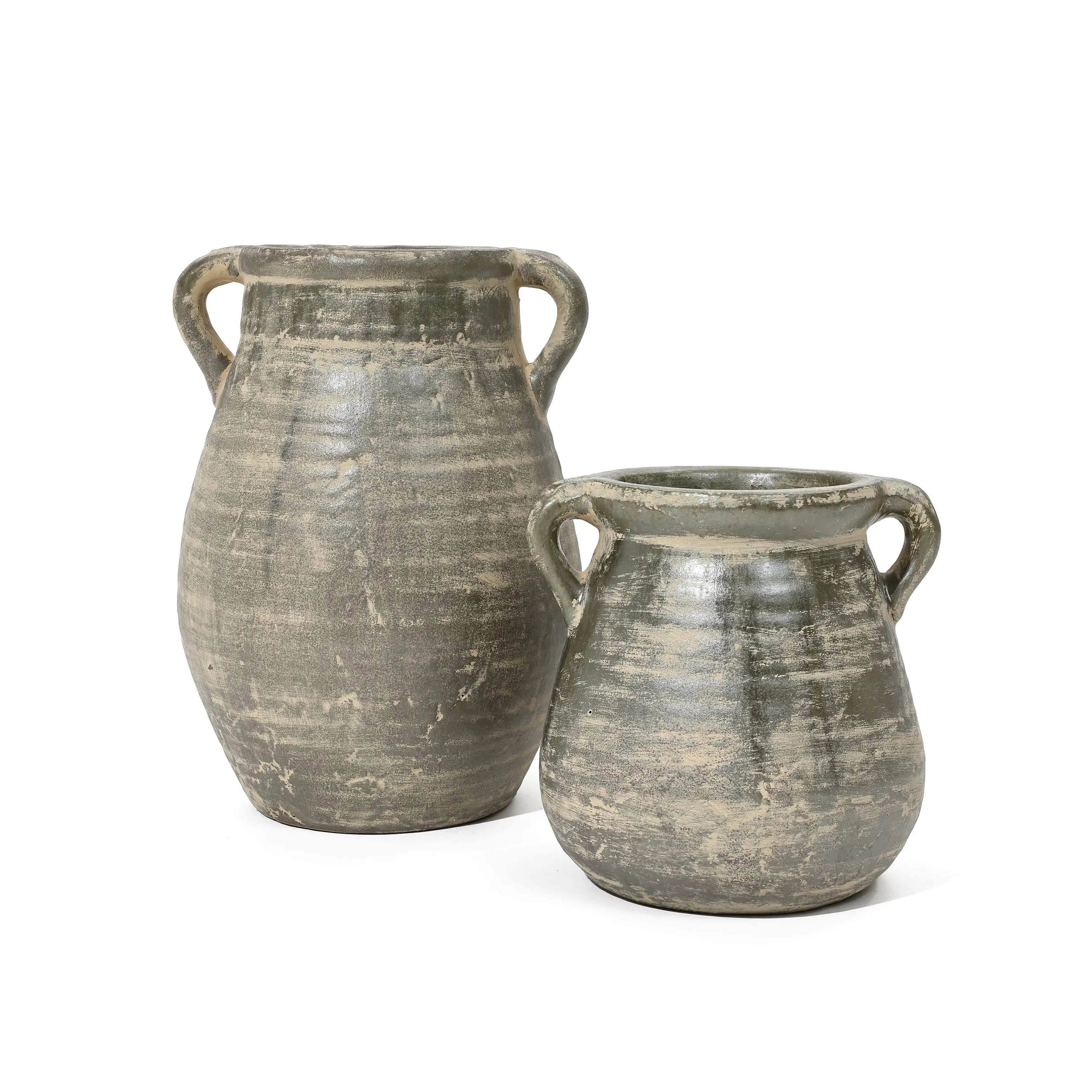 Two handcrafted, rustic green-gray clay pots with handles, one larger and the other smaller, stand side by side against a plain white background. These vessels evoke a sense of historic depth reminiscent of ancient terracotta jug vases.