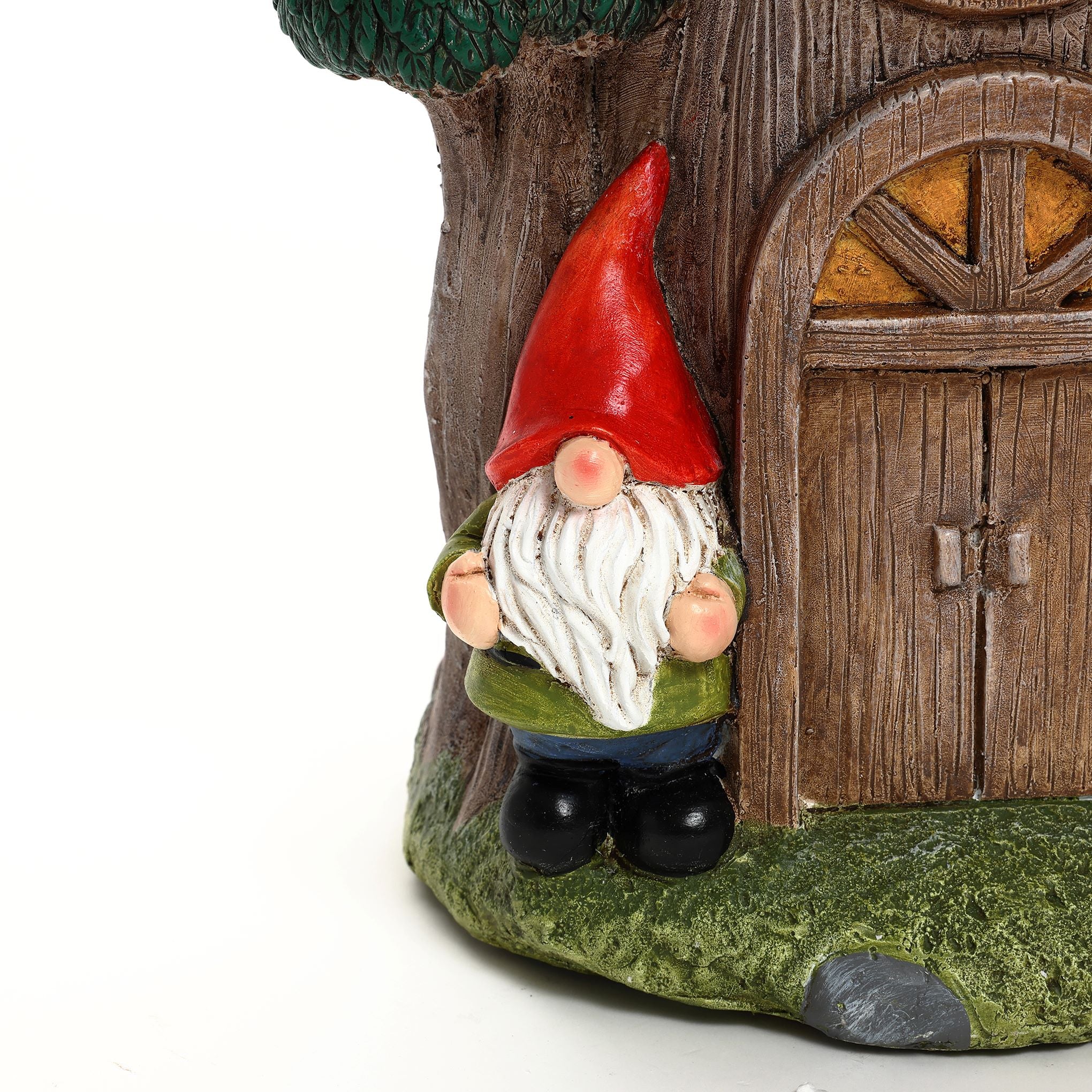 A garden gnome figurine with a red hat and white beard stands next to a charming gnome tree house with a wooden door, making it a delightful addition to your outdoor space decor.