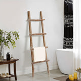 A solid wood blanket ladder leans against the wall, exuding rustic charm as it holds a white towel. The decor includes a lush plant and a wooden table adorned with candles. Nearby, a bathtub sits gracefully with its patterned black and white curtain, blending modern functionality with timeless design.