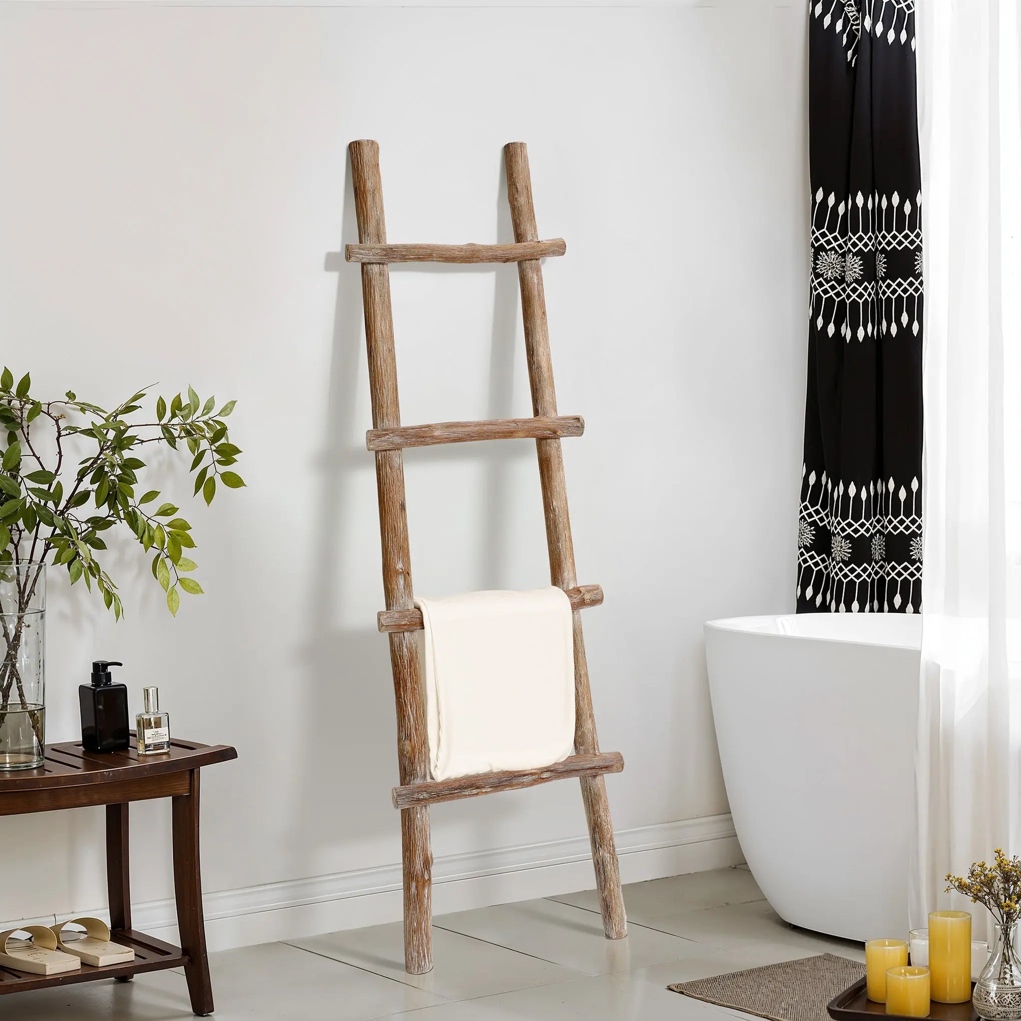 A solid wood blanket ladder leans against the wall, exuding rustic charm as it holds a white towel. The decor includes a lush plant and a wooden table adorned with candles. Nearby, a bathtub sits gracefully with its patterned black and white curtain, blending modern functionality with timeless design.