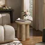 A manufactured wood side table with a pink rose bouquet in a glass vase, a candle, and books is nestled next to a beige sofa in a sunlit room.