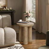 A manufactured wood side table with a pink rose bouquet in a glass vase, a candle, and books is nestled next to a beige sofa in a sunlit room.