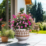 A large decorative round planter crafted from magnesium oxide, brimming with vibrant pink and white flowers, graces the patio next to a smaller pot, evoking a hint of Bohemian style amid trees and a house in the background.