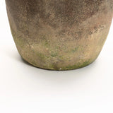 Close-up of a handcrafted ceramic pot with a weathered finish, showing its textured surface and patches of green moss at the base. Ideal as an indoor and outdoor urn, this rustic terracotta piece adds charm to any garden or home setting.