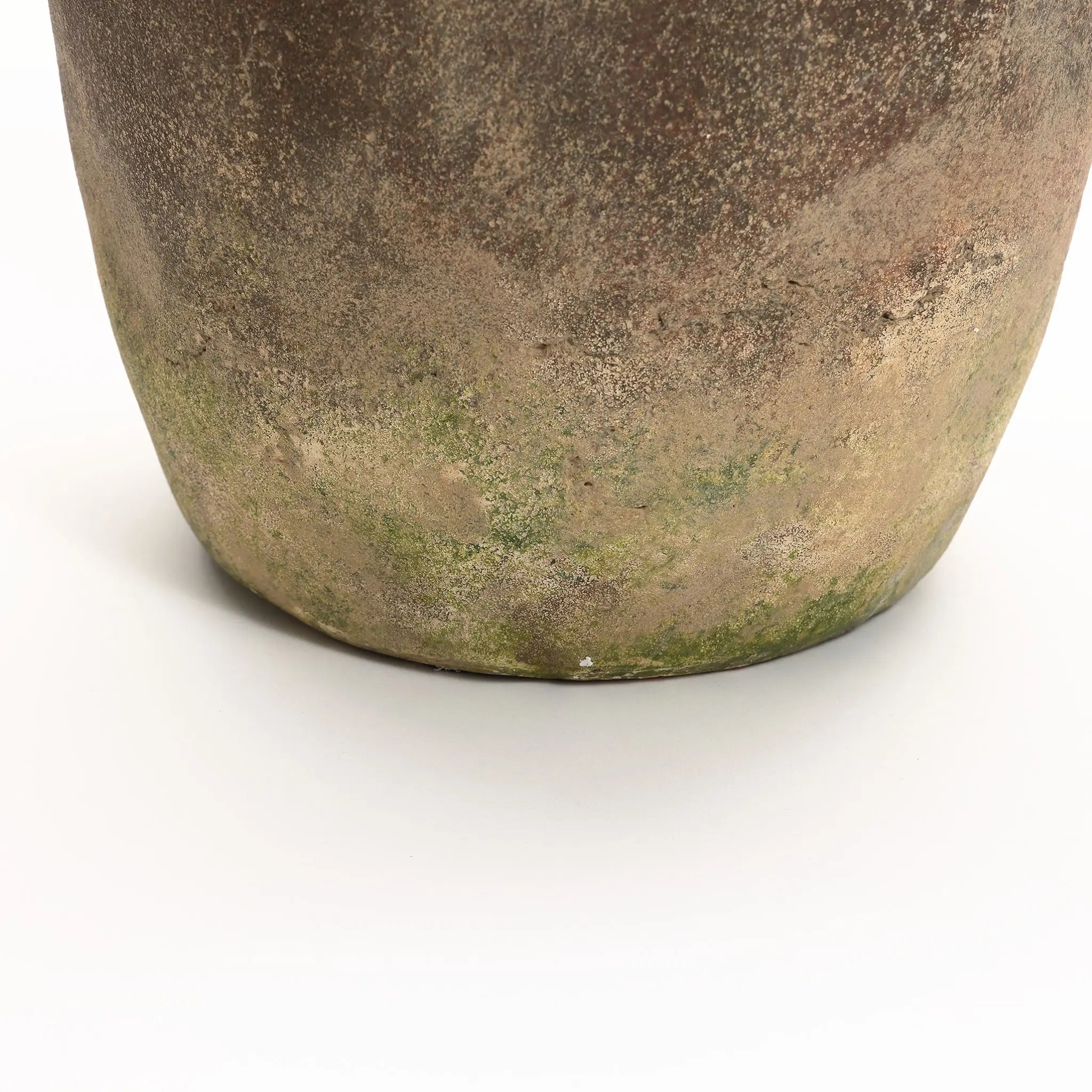 Close-up of a handcrafted ceramic pot with a weathered finish, showing its textured surface and patches of green moss at the base. Ideal as an indoor and outdoor urn, this rustic terracotta piece adds charm to any garden or home setting.