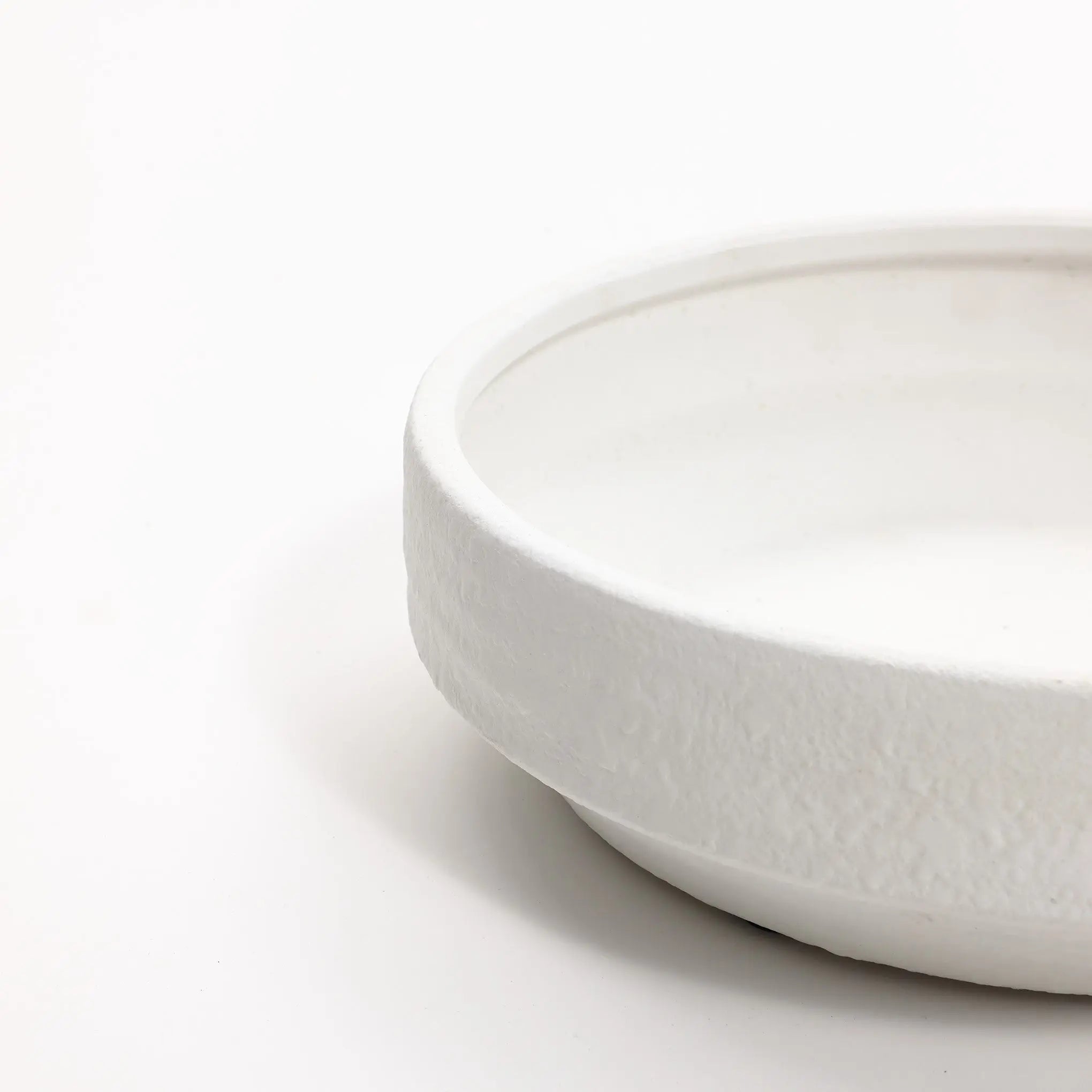 Close-up of a white terracotta vase with a textured exterior surface, reminiscent of a round bowl, set against a plain white backdrop.