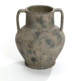 A Rustic mottled grey terracotta urn vase with handles by LuxenHome, measuring 12.1 high, sits on a plain white background. Its weathered surface features darker spots and rustic design elements, suggesting antiquity and historical value.