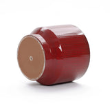 A LuxenHome burgundy red glazed round ceramic planter, 10.83 high, lies on its side against a white background. This elegant decoration features a glossy finish and an unfinished base with a drainage hole.