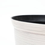 Close-up of a textured, light-colored round plastic planter with a black interior edge, showcasing its durable construction against a plain white background.