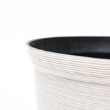 Close-up of a textured, light-colored round plastic planter with a black interior edge, showcasing its durable construction against a plain white background.