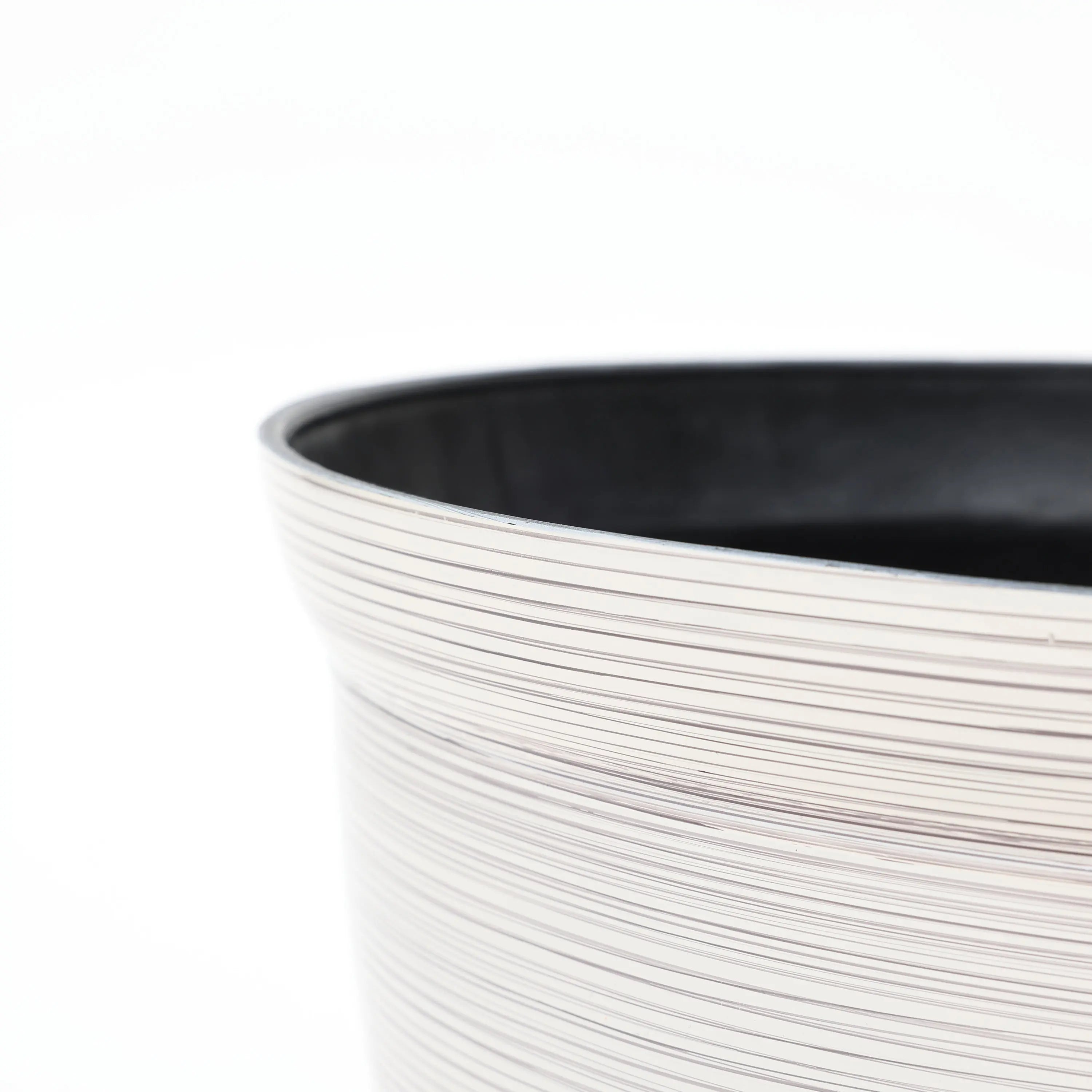 Close-up of a textured, light-colored round plastic planter with a black interior edge, showcasing its durable construction against a plain white background.