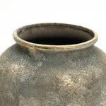Close-up of a LuxenHome Rustic Gold and Brown Terracotta Urn Vase, 15.2 h, with an aged texture in gray and brown. The wide, uneven rim and rounded shape are highlighted by lighting that accentuates its charmingly rustic appearance through antique distressing techniques.