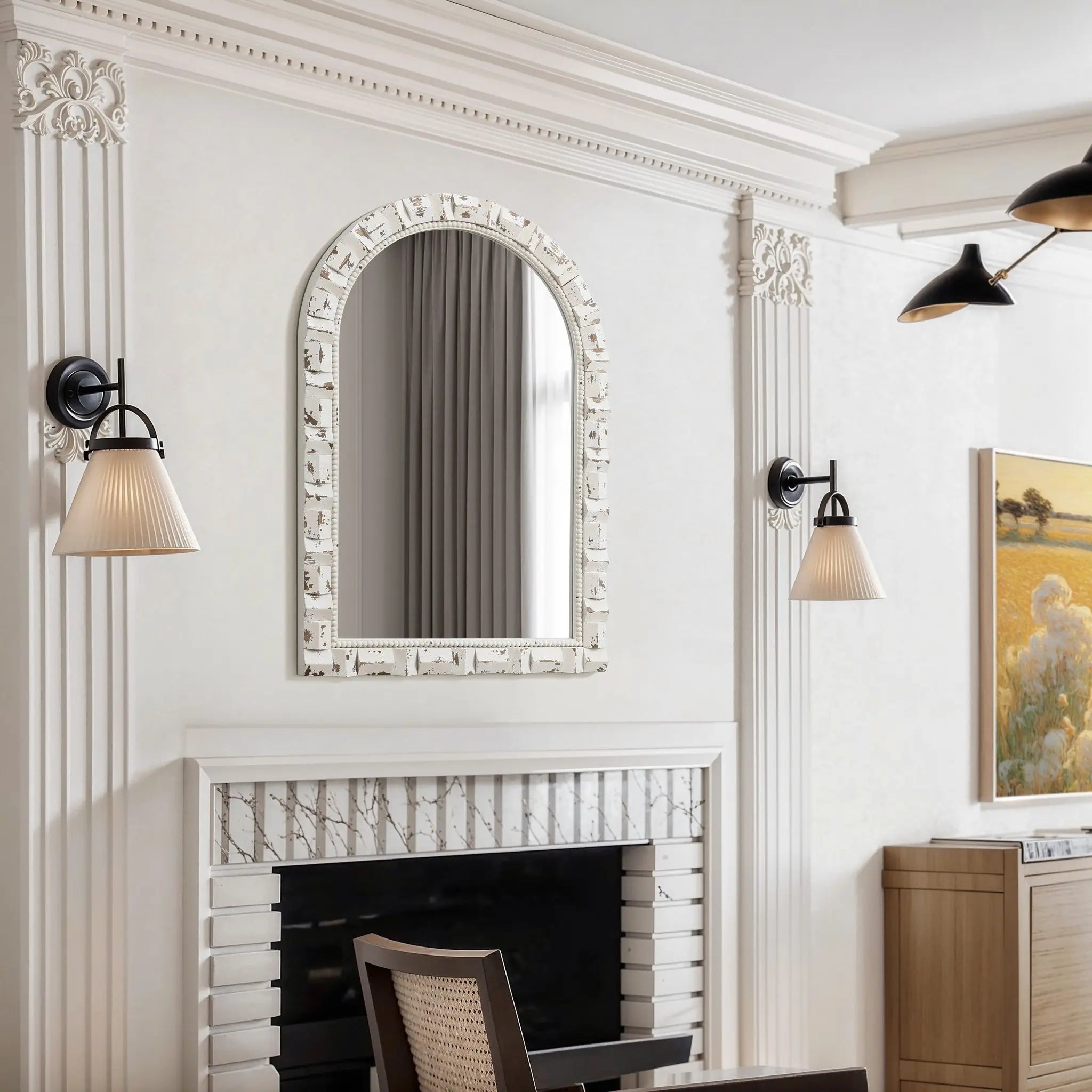 Elegant living room featuring a decorative fireplace, vintage wall mirror, wall sconces, and artwork depicting a pastoral scene. Neutral color palette with white walls and black accents enhances the timeless charm of this exquisite space.
