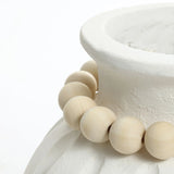A close-up of a modern round vase featuring a vertical ribbed design, with large, round wooden beads elegantly draped around its neck.