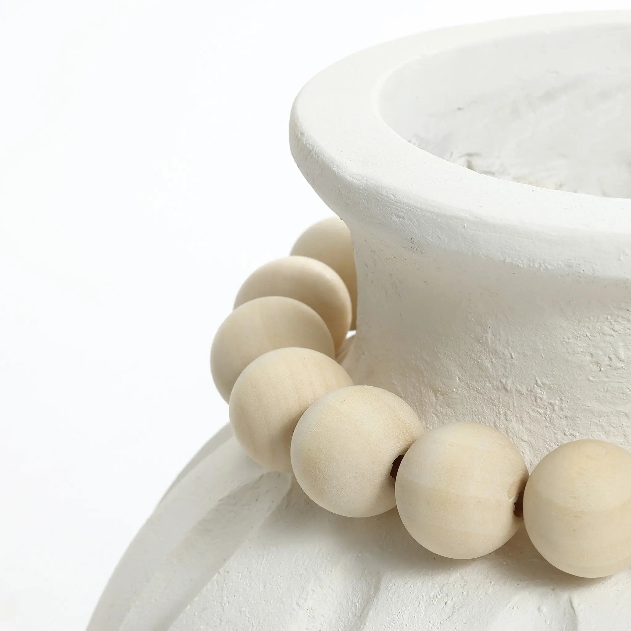 A close-up of a modern round vase featuring a vertical ribbed design, with large, round wooden beads elegantly draped around its neck.