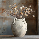 A LuxenHome rustic gray and white terracotta vase with handles, standing 11 inches high, holds a bouquet of dried white flowers on a wooden surface. The weathered background enhances the contemporary elegance of the vintage scene.
