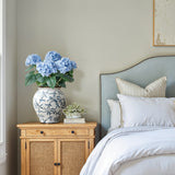 With a Floral Ceramic Vase of hydrangeas, a small white flower arrangement, and books beside a neatly made bed.
