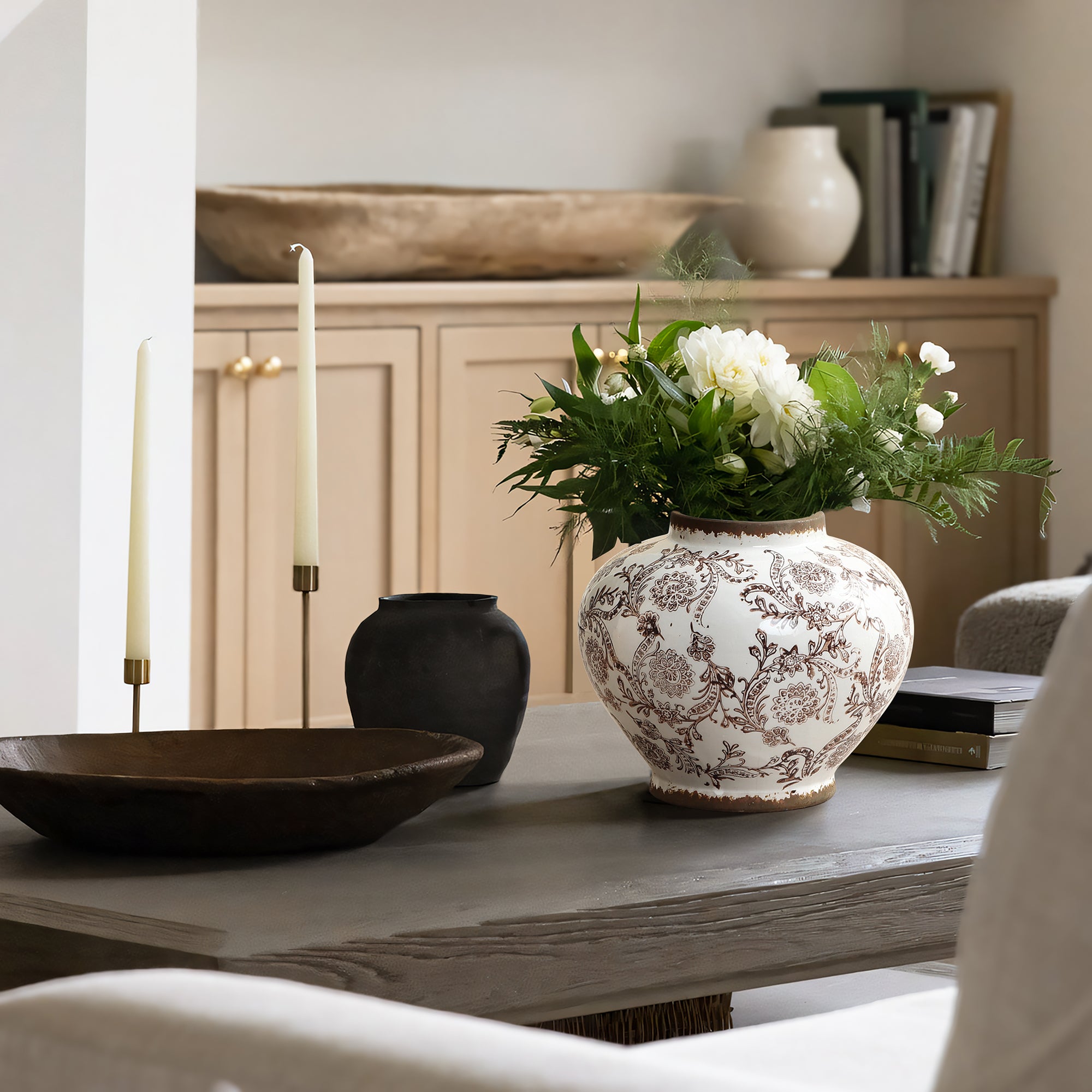 Elegant vase with white flowers and greenery sits on a wooden coffee table, adding timeless charm to the home décor.