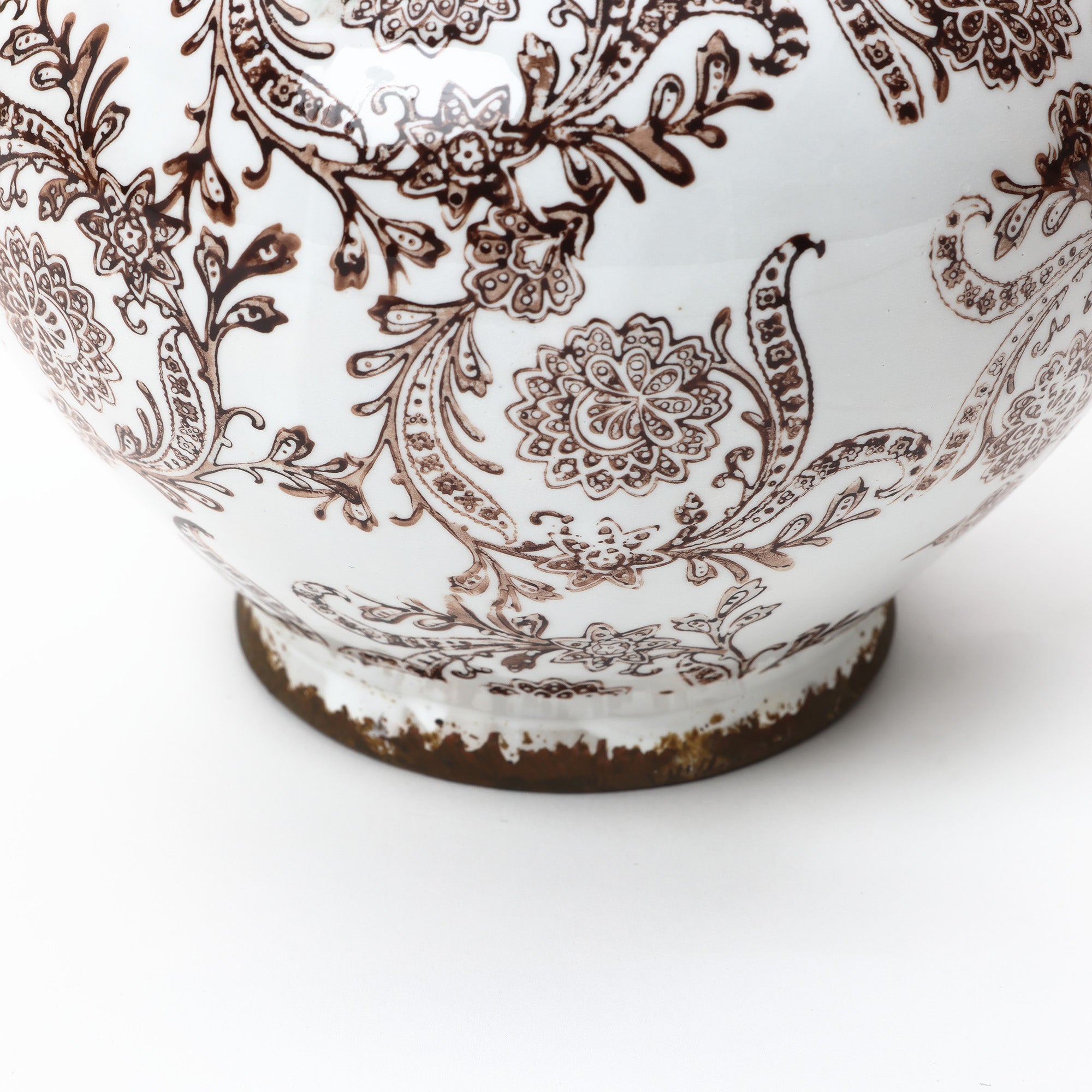 Close-up of ceramic vase adorned with intricate brown floral and paisley patterns, showing some wear around the base.