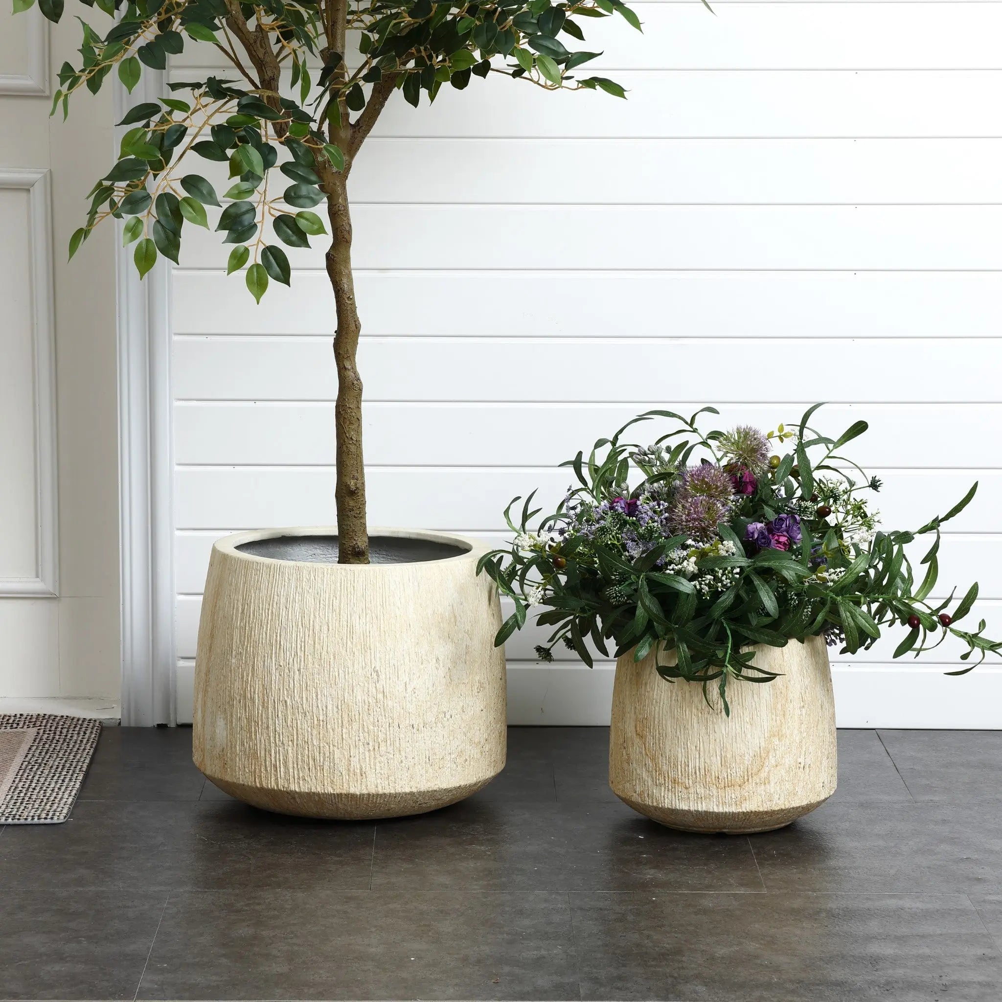 Two beige ceramic pots with ribbed texture sit on a dark floor; one nurtures a tree with green leaves, the other cradles vibrant flowering plants. The serene scene is set against white wooden paneling, perfect for both indoor and outdoor settings.