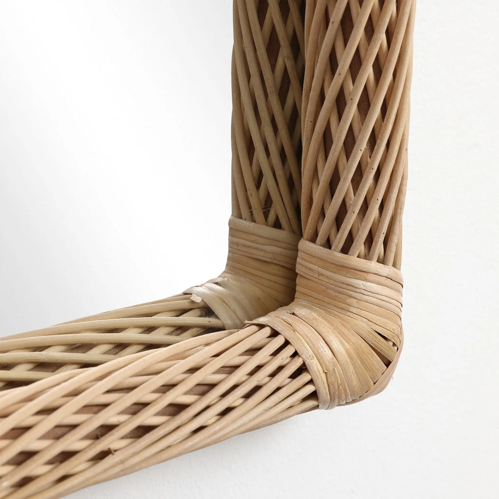 Close-up of a wicker basket corner, showcasing an interwoven pattern of light brown rattan strands, reminiscent of the intricate design found in a bamboo-framed mirror.