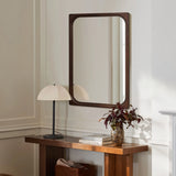 A wooden console table with a rubberwood frame stands against a white wall, featuring a potted plant, small lamp, and two stacked books. Above it hangs a stylish rectangular wall mirror, perfecting this elegant piece of home decor.