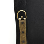 A close-up of a leather strap with an antique brass D-ring and three black screws, secured to a sleek black frame, embodies modern minimalism.