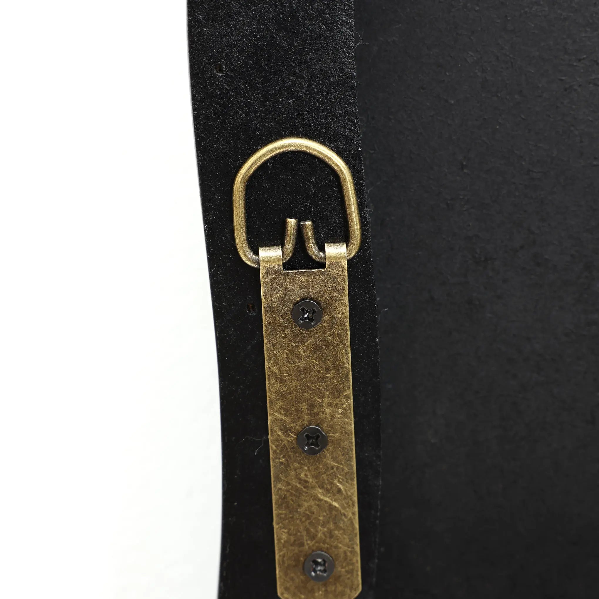 A close-up of a leather strap with an antique brass D-ring and three black screws, secured to a sleek black frame, embodies modern minimalism.