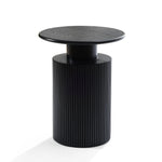 A black cylindrical side table with a ribbed base and smooth round top showcases a modern aesthetic against a white background, accented by hints of natural wood grain.