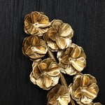 A cluster of intricately designed gold orchids, resembling exquisite flower bouquets, is artfully arranged on a textured black surface, creating a stunning piece of wall art.