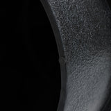 Close-up of a textured, curved, dark green metal surface featuring a unique white irregular pattern, with a small circular detail, set against a black background.