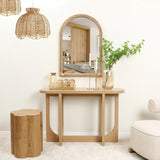 A wooden console table sits below a bamboo-framed mirror, flanked by glass vases and candles. A wooden stool and wicker pendant lights complete the decor. The room feels light and airy with its neutral color scheme, adding a touch of warmth to the serene ambiance.