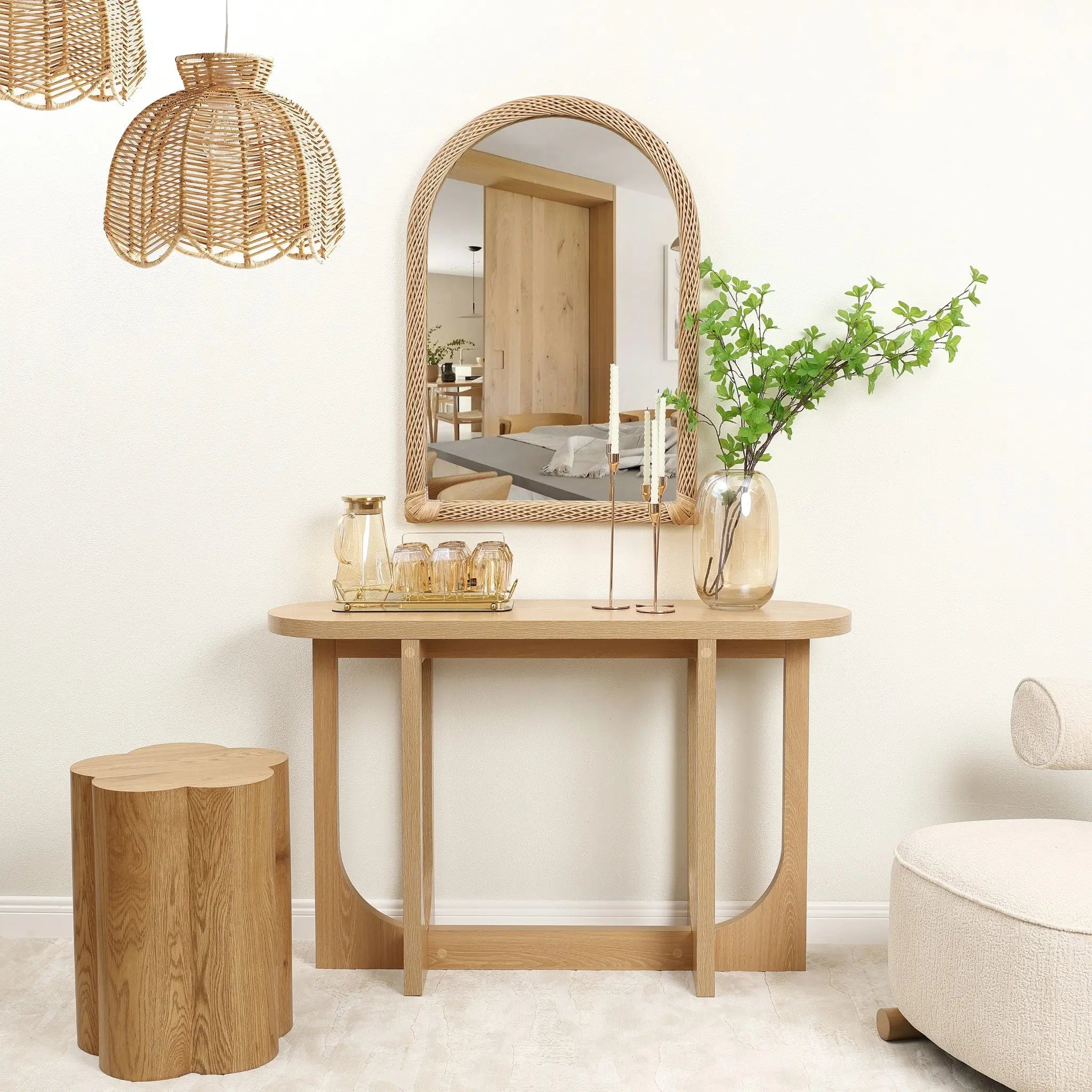 A wooden console table sits below a bamboo-framed mirror, flanked by glass vases and candles. A wooden stool and wicker pendant lights complete the decor. The room feels light and airy with its neutral color scheme, adding a touch of warmth to the serene ambiance.