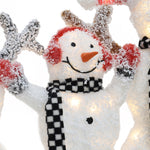 A charming snowman decoration with red earmuffs, a black and white checkered scarf, and arms raised, covered in artificial snow—perfect for your outdoor Christmas decor.