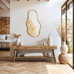 A minimalist living space features a wooden console table with vases and an irregular oval-shaped mirror as a decorative statement. Sunlight streams through a large window, illuminating the wicker pouf and highlighting elements of natural pine wood.