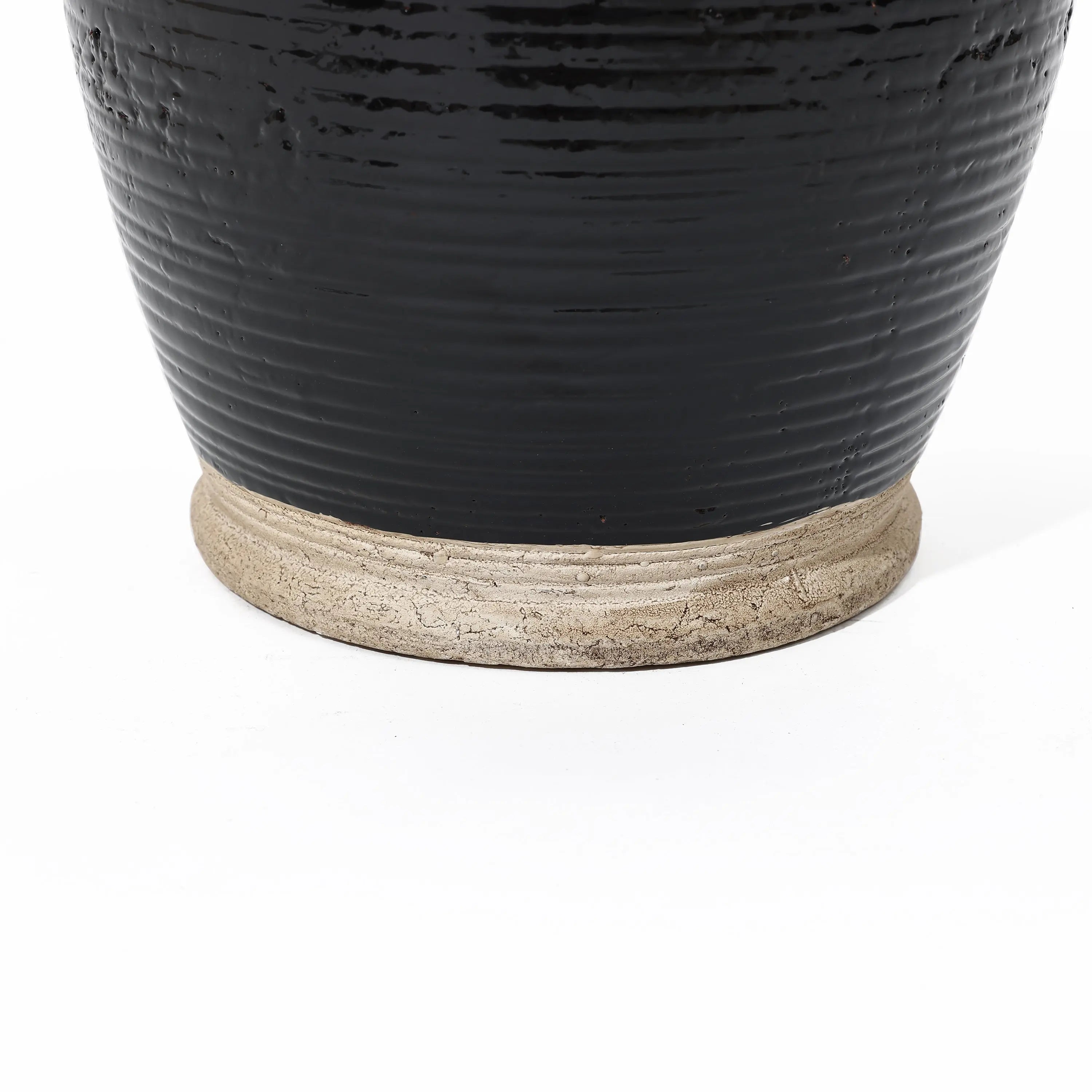 Close-up of a dark, glossy ceramic pot with black glaze and a rough, unglazed base on a white background, showcasing its handcrafted artistry.