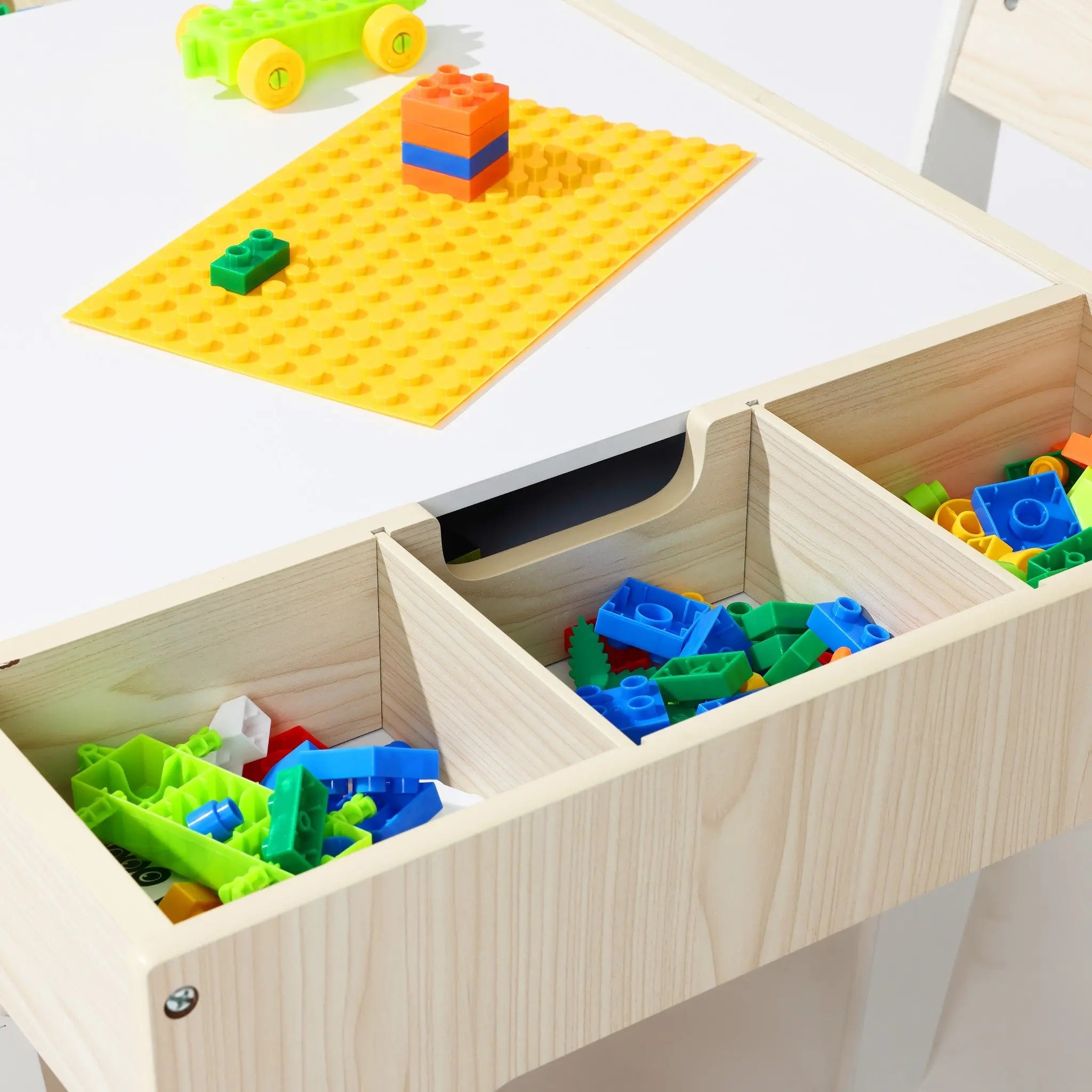 The LuxenHome Drawing and Activity Board Children Table with 2 Chairs Set features open storage showcasing colorful building blocks, including a green toy car, a yellow baseplate with stacked blocks, and is multi-functional furniture perfect for play and creativity.