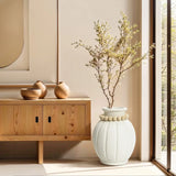 Minimalist room with a wooden console table, ceramic vases, and a large modern round vase holding delicate branches. The vertical ribbed design subtly accentuates the space as sunlight streams in through a nearby window.
