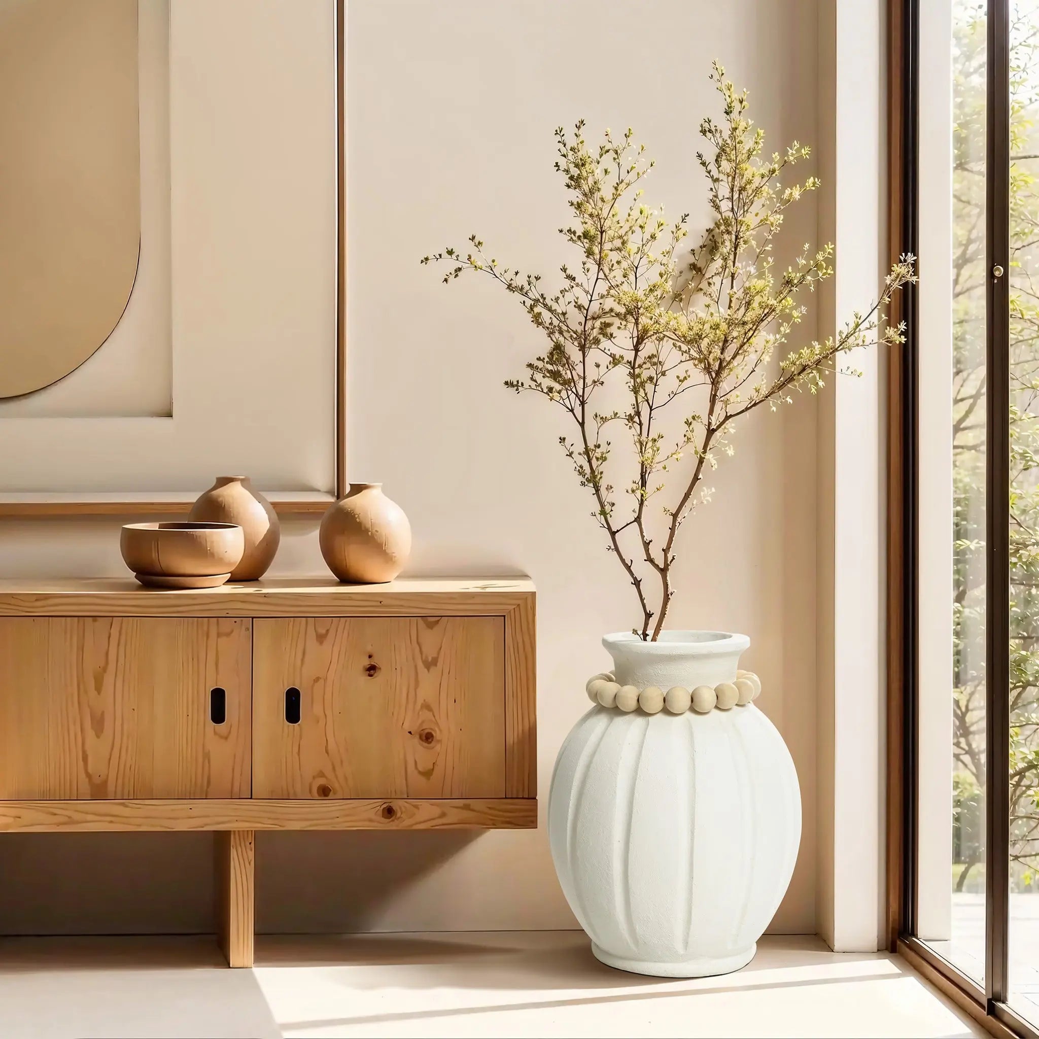 Minimalist room with a wooden console table, ceramic vases, and a large modern round vase holding delicate branches. The vertical ribbed design subtly accentuates the space as sunlight streams in through a nearby window.