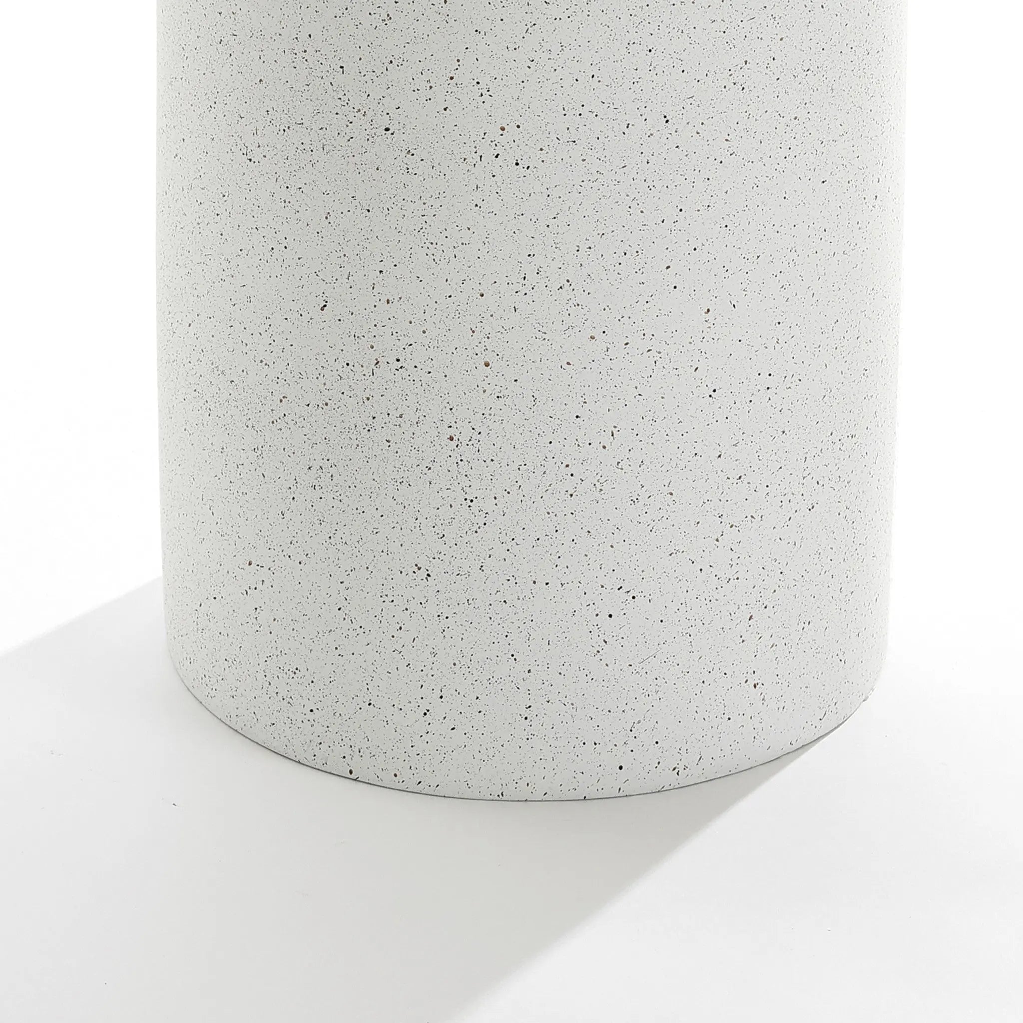 A close-up of the Speckled white pillar outdoor side table reveals its white, speckled surface. Made from durable MGO material, it features a smooth texture that casts a soft shadow, adding contemporary flair and making it perfect for modern outdoor settings.